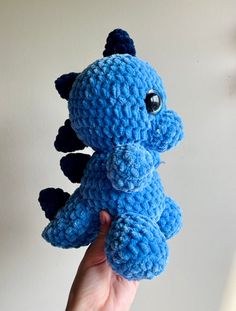 a blue crocheted dragon stuffed animal held up in the air by someone's hand