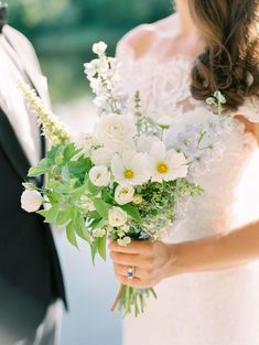 a bride and groom standing next to each other in front of a lake holding flowers