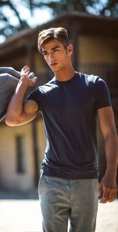 a young man is holding his hat and looking at the camera while standing in front of a house