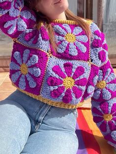 a woman sitting on the ground wearing a purple and yellow crocheted sweater with flowers