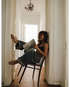 a woman is sitting in a chair reading a newspaper and smiling at the camera while holding her leg up