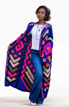 a woman is standing in front of a white background wearing a colorful crochet blanket