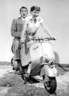 a man and woman riding on the back of a scooter in the desert