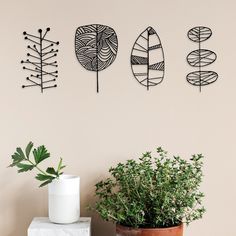 three metal art pieces hanging on the wall next to a potted plant and vase