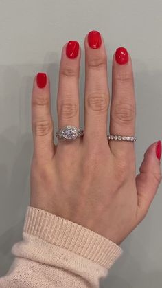 a woman's hand with red nail polish and a diamond ring on her finger