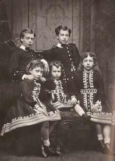 an old black and white photo of four children in fancy dress clothes, posing for a family portrait