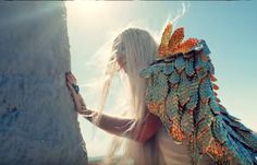 a woman with long white hair and wings on her head standing next to a pillar