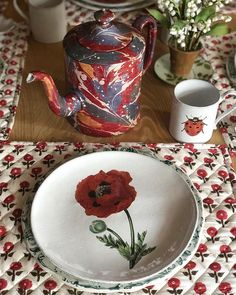 a red flower painted on the side of a white plate next to a teapot