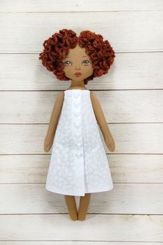 a doll with red hair wearing a white dress and standing on a wooden floor next to wood planks