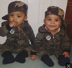 two small children sitting on the floor in camouflage outfits