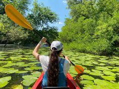 a woman in a red kayak paddles through the water with lily pads on it