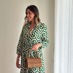 a woman in a green and white dress holding a brown purse standing next to a window