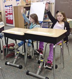 children sitting at desks with their arms in the air