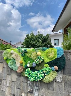 a wall covered in green and blue flowers next to a building with trees on it