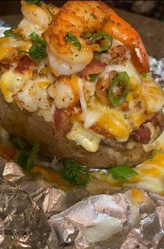 a loaded baked potato with shrimp and cheese on it is sitting on foil covered table