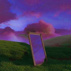 there is a mirror in the middle of a grassy field with purple clouds behind it