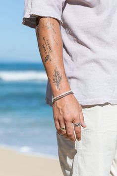 a man with a tattoo on his arm walking along the beach