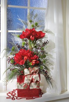 a vase filled with red flowers on top of a window sill next to a christmas decoration