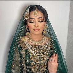 a woman in a green and gold bridal outfit with jewelry on her head, wearing a veil