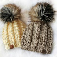 two knitted hats with faux fur pom - poms on top of each other