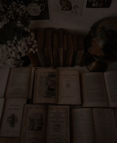 an arrangement of old books on a table with flowers in the corner and pictures above them