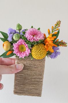 a hand holding a vase with flowers in it