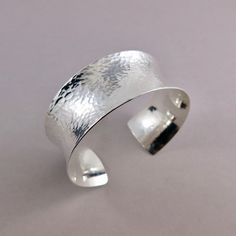 Add a touch of luxury to your jewelry collection with the Wide Concave Silver Cuff Bracelet. Expertly handcrafted from sterling silver in a wide concave shape, this bracelet has been carefully textured by hand and is incredibly comfortable to wear. Enjoy the fine details of this timeless piece and make a bold statement. Cuff is adjustable by squeezing the gap together or pulling it apart.     Product Details: * This cuff bracelet is made to order.  Will ship within 5 business days of order. * St Elegant Hammered Cuff Bangle, Sterling Silver Cuff Bracelet With Polished Finish, Sterling Silver Jubilee Cuff Bracelet, Luxury Silver Open Cuff Bracelet, Silver Open Cuff Bracelet With Polished Finish, Elegant Sterling Silver Cuff Bangle, Luxury Silver Open Cuff Bracelets, Silver Hammered Cuff Bracelet, Hammered Bangle Cuff Bracelet For Anniversary