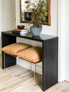 a black console table with two pillows and a plant on top, in front of a mirror