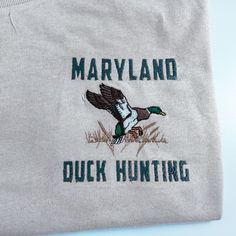 Discover the perfect shirt to capture your passion for Maryland Duck Hunting! Crafted from 100% cotton, this unisex design features a striking embroidery of the state's signature duck hunting. Get ready to show off your enthusiasm in style! Available in short sleeve, long sleeve, and crewneck 100% cotton Color is Sand Unisex Sizing Professionally Embroidered Fall Embroidered Graphics Cotton T-shirt, Fall Cotton T-shirt With Embroidered Graphics, Custom Embroidery Short Sleeve T-shirt, Fall Short Sleeve T-shirt With Embroidered Logo, Fall Embroidered Graphics Short Sleeve T-shirt, Fall Embroidered Short Sleeve T-shirt, Hunting Embroidery, Embroidered Things, Duck Hunting Shirts