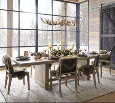 a dining room table with chairs, candles and deer antlers hanging from the ceiling