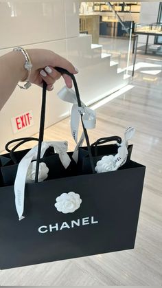 a person holding a chanel bag in their hand and some white ribbons on it