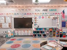 a classroom with lots of desks, chairs and a large television mounted to the wall