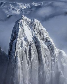 the top of a mountain covered in snow with clouds around it and an airplane flying overhead