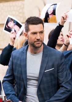 a man in a suit holds up photos and looks at the camera while surrounded by other people