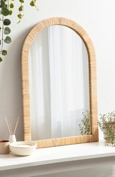 a mirror sitting on top of a white shelf next to a potted plant and bowl