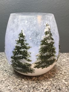 a glass with trees painted on it sitting on top of a granite counter next to a gray wall