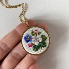 a hand holding a cross stitch necklace with flowers on it