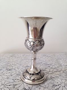 a silver vase sitting on top of a table next to a lace covered tablecloth