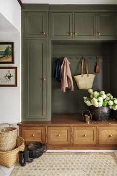 an entryway with green cabinets and white flowers in a basket on the bench next to it