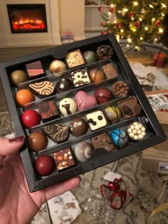 a person holding a box filled with chocolates in front of a christmas tree