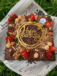 a birthday cake with nuts, chocolate and strawberries on it sitting in the grass