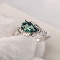 a ring with an oval cut green stone surrounded by diamonds on a white cloth background