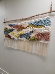 a wall hanging made out of different colored beads and yarns on a white wall