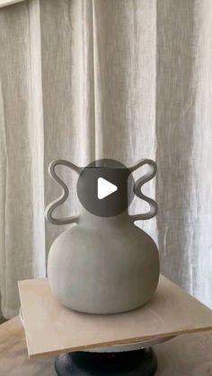 a white vase sitting on top of a wooden table next to a drapesed window