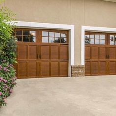 two brown garage doors in front of a tan building with pink flowers on the side