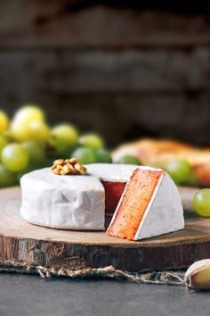 a piece of cake sitting on top of a wooden board next to grapes and nuts