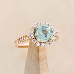 a ring with an aqua blue topaz surrounded by white and yellow diamonds on a wooden stand