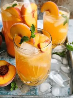 two glasses filled with ice and peaches next to sliced peaches on a tray