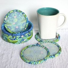 three coasters and a coffee cup on a white table cloth with a mug in the middle