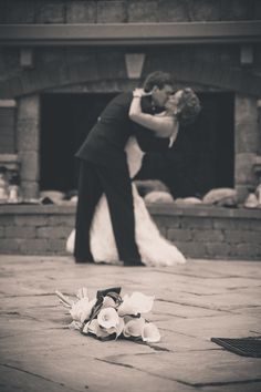 a bride and groom kissing in front of a fire place with flowers on the ground